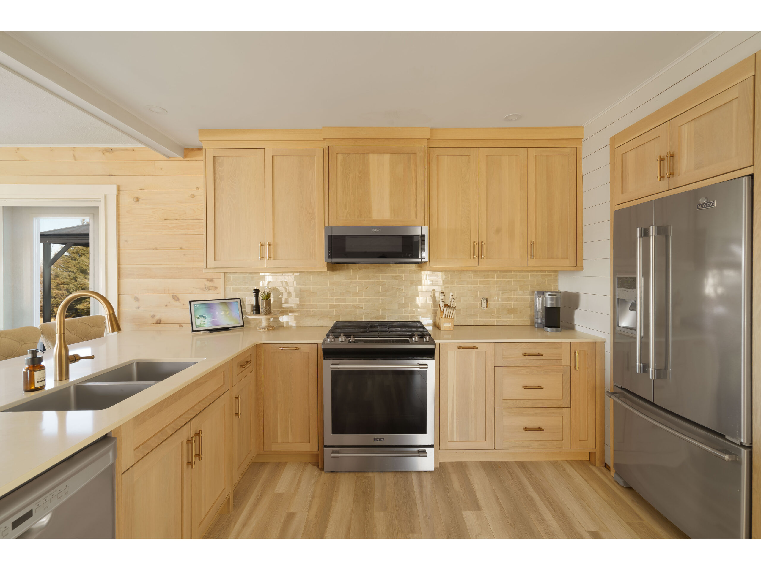 A small but open kitchen with a large peninsula and barstools, wooden cabinets that match the wood-panelled wall, and stainless steel appliances.