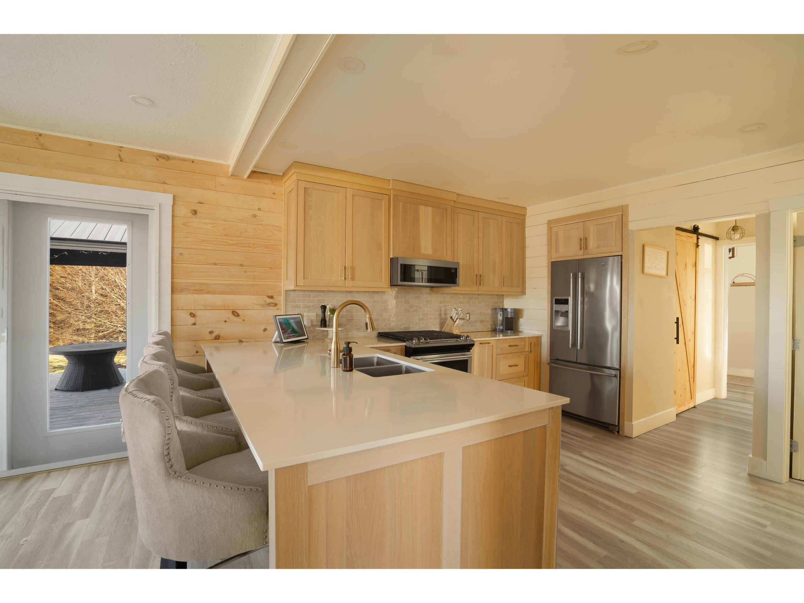 A small but open kitchen with a large peninsula and barstools, wooden cabinets that match the wood-panelled wall, and stainless steel appliances.