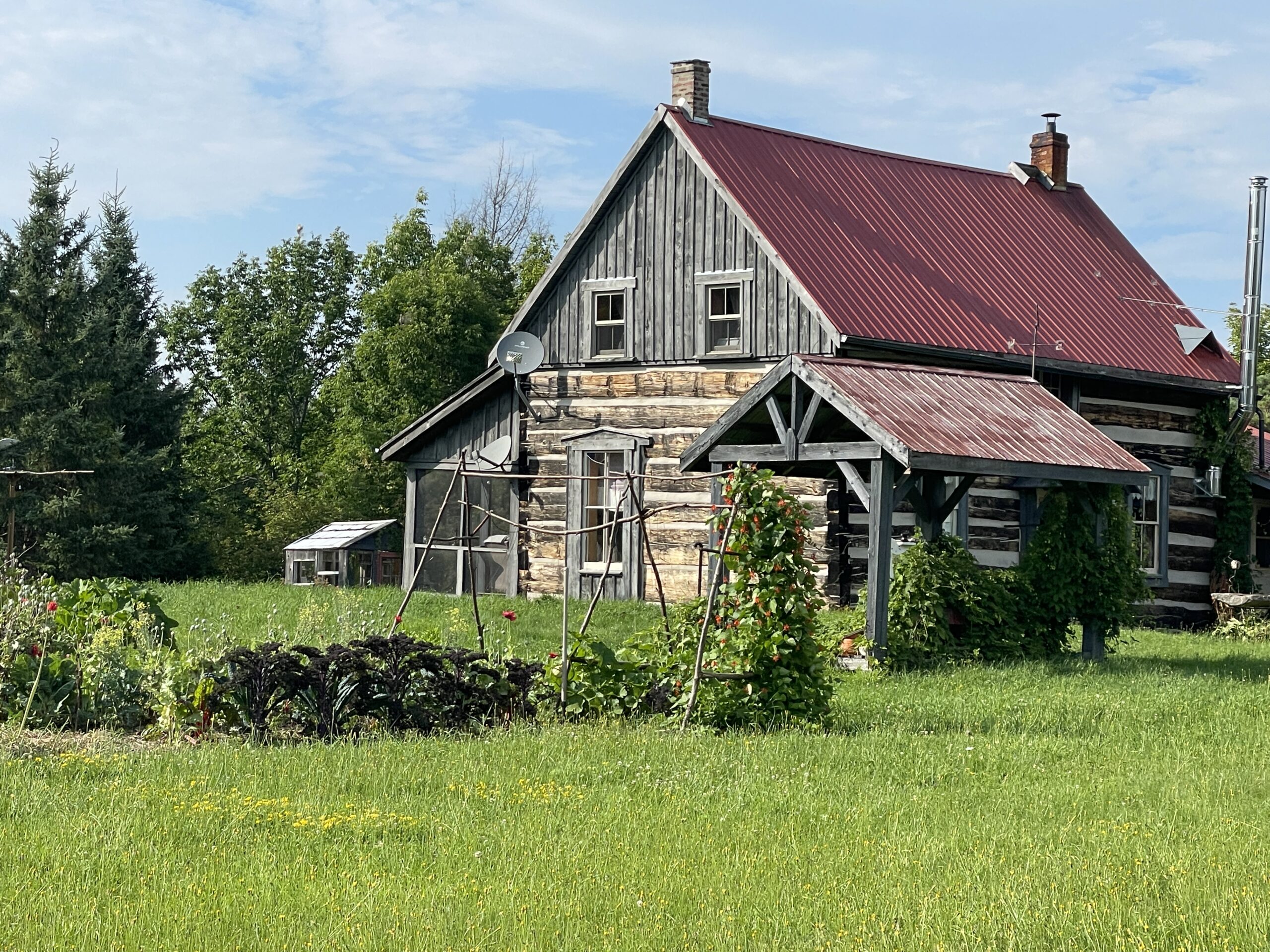A farmhouse sits in a green field, with trees beyond.