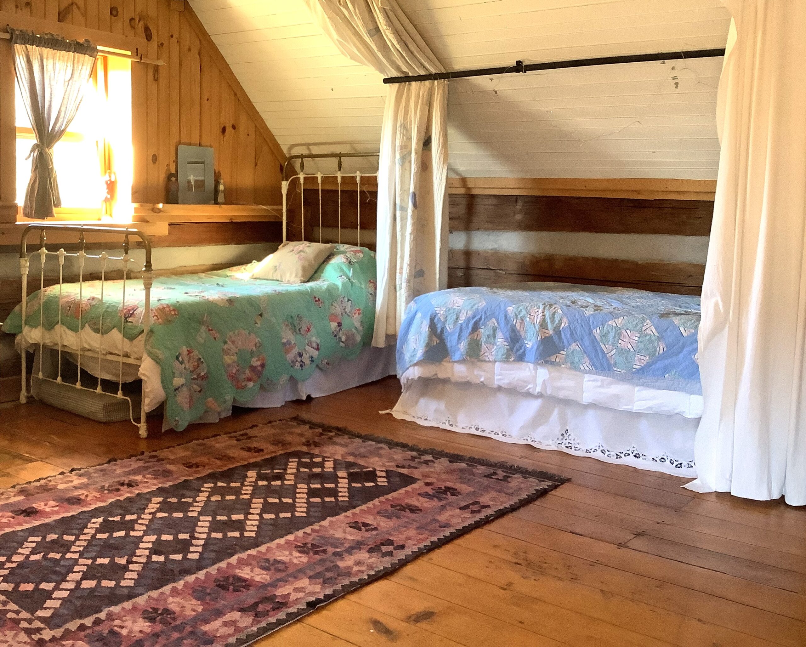 A big bedroom with angled walls, two perpendicular single beds, and ornate area rug over hardwood flooring, and a window.