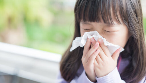 A young girl blowing her nose in front of a window