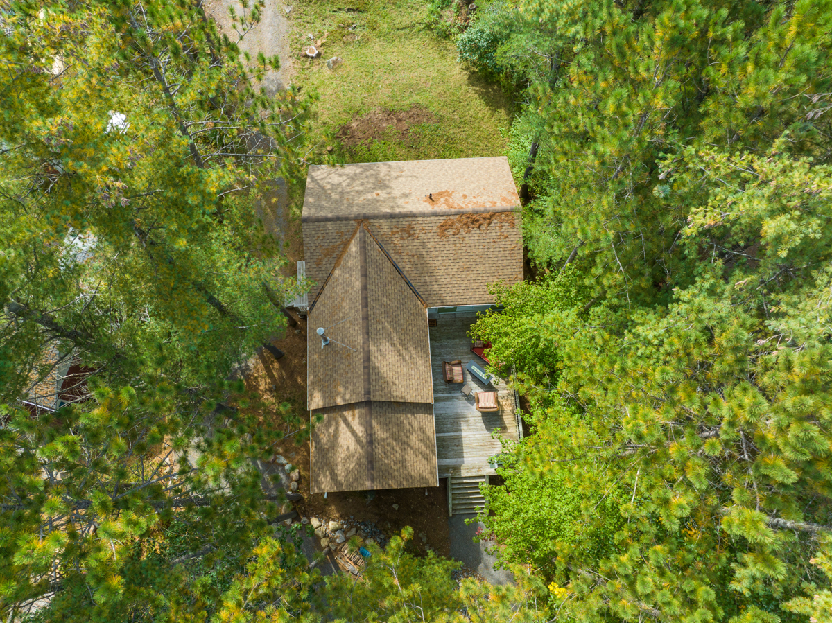 Aerial view of a cottage with light brown wood shingles and a deck.