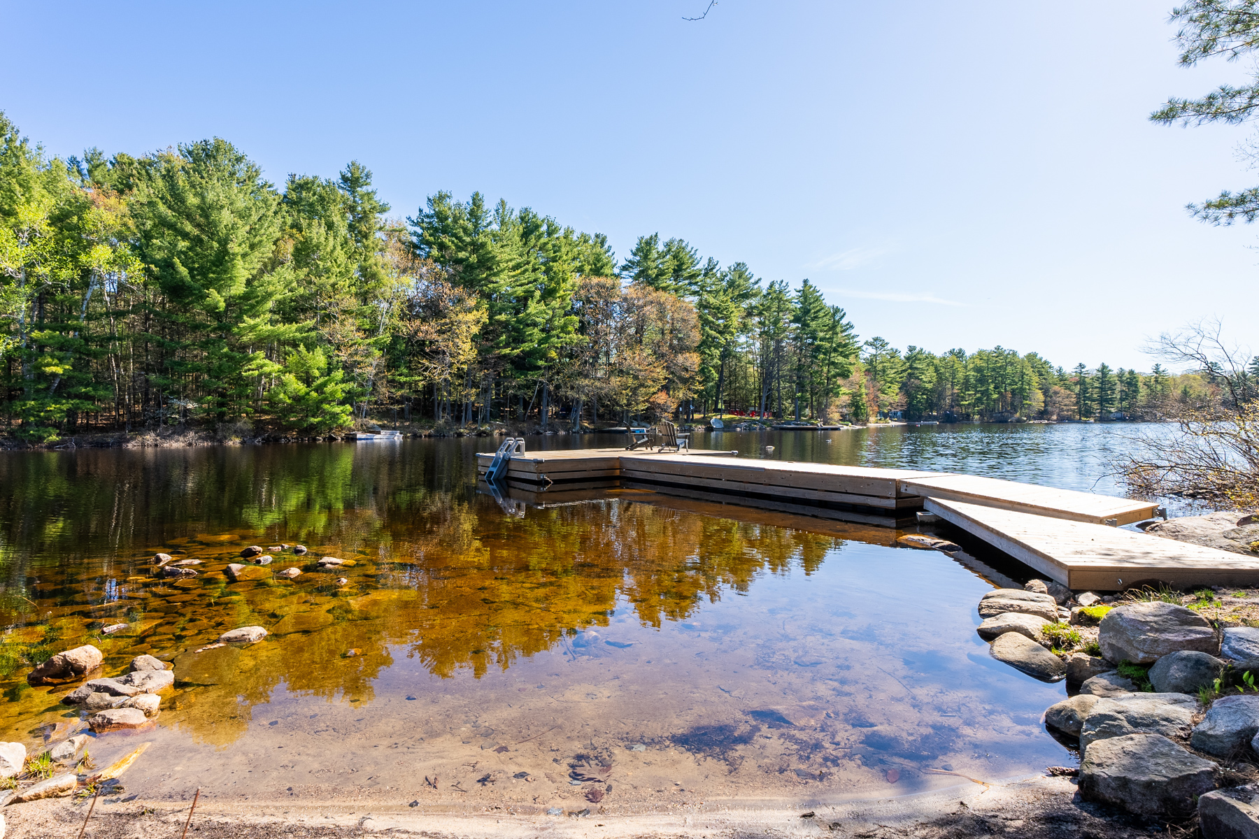 A huge dock extends in a curve into a calm lake. The water at the shoreline is shallow.