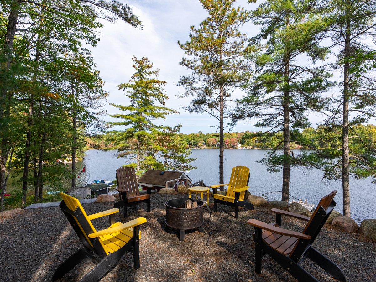 A fire pit surrounded by black and yellow chairs overlooks the lake