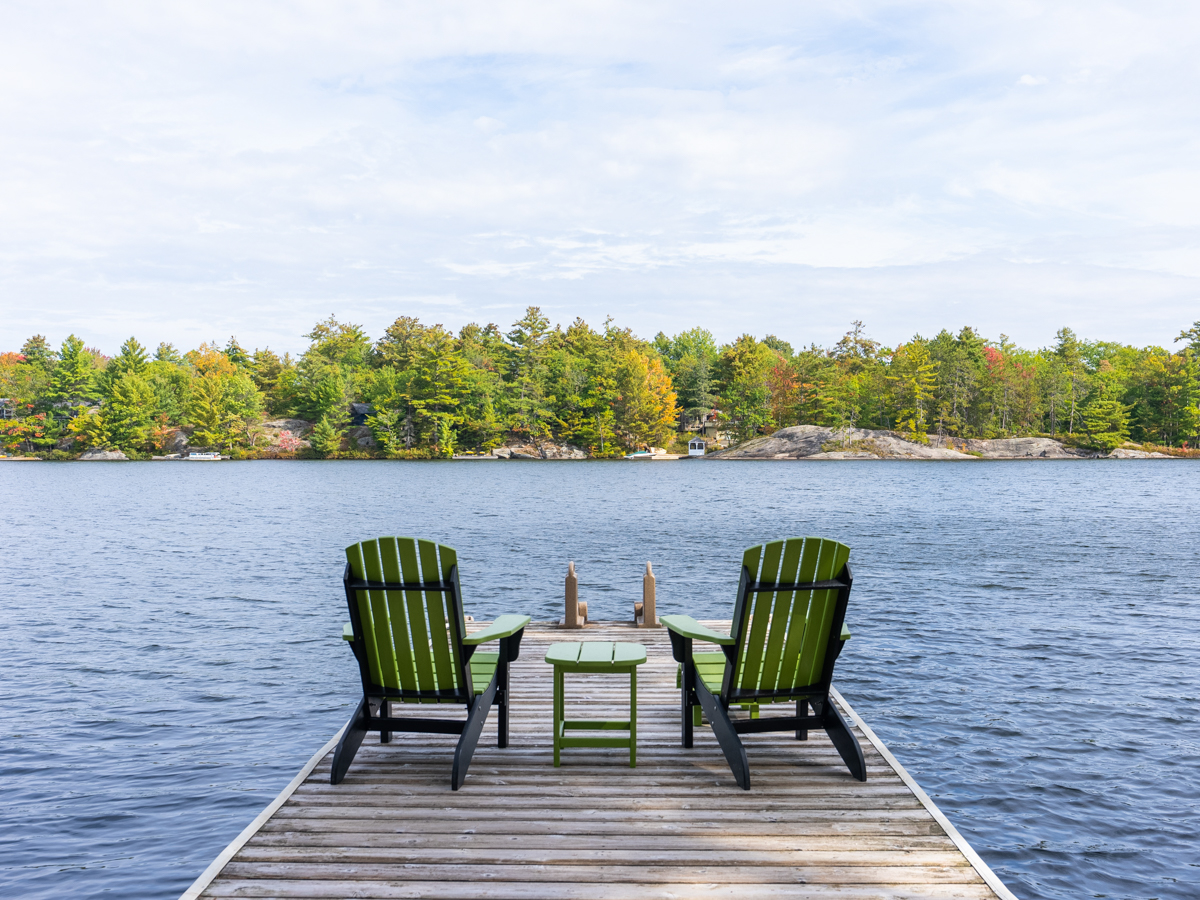 Two green Muskoka chairs on a dock face out towards the lake