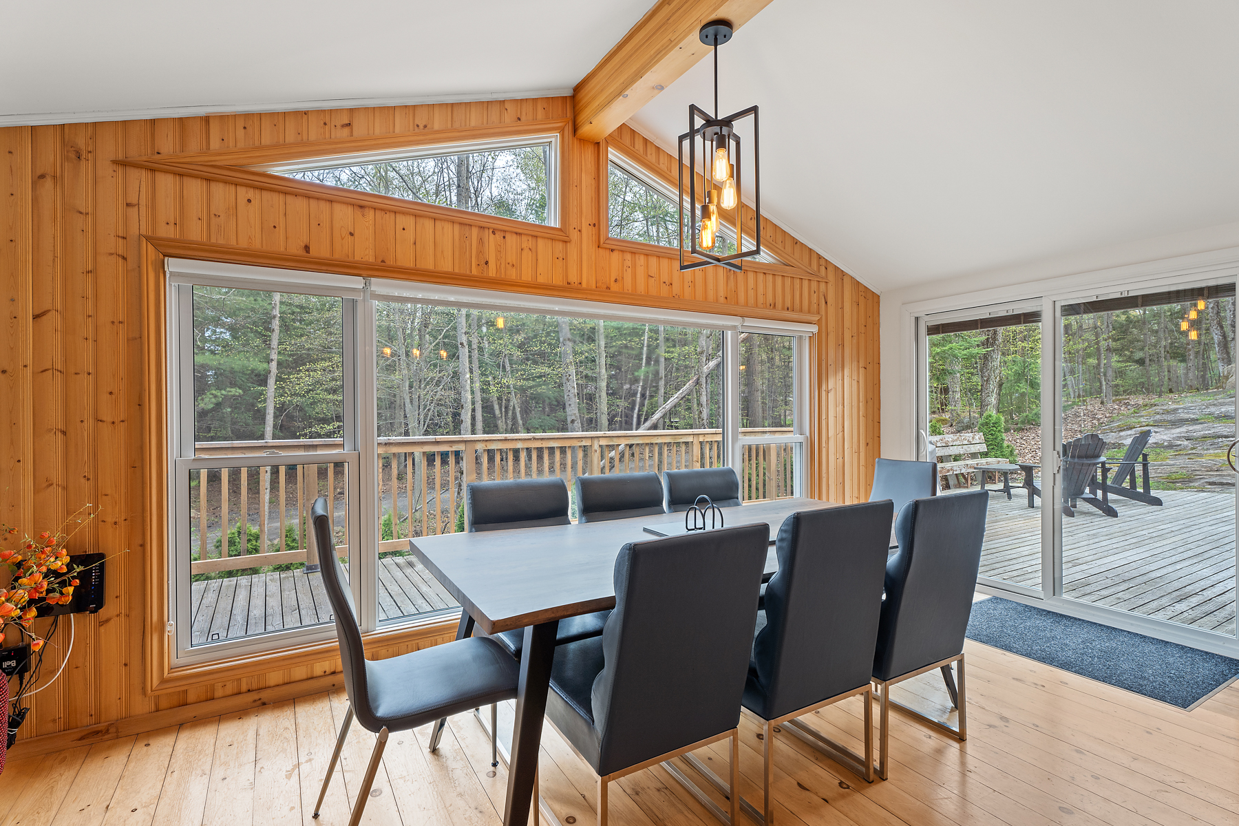 A big dining table and chairs sit in front of a wall of windows, which look out to a big deck.