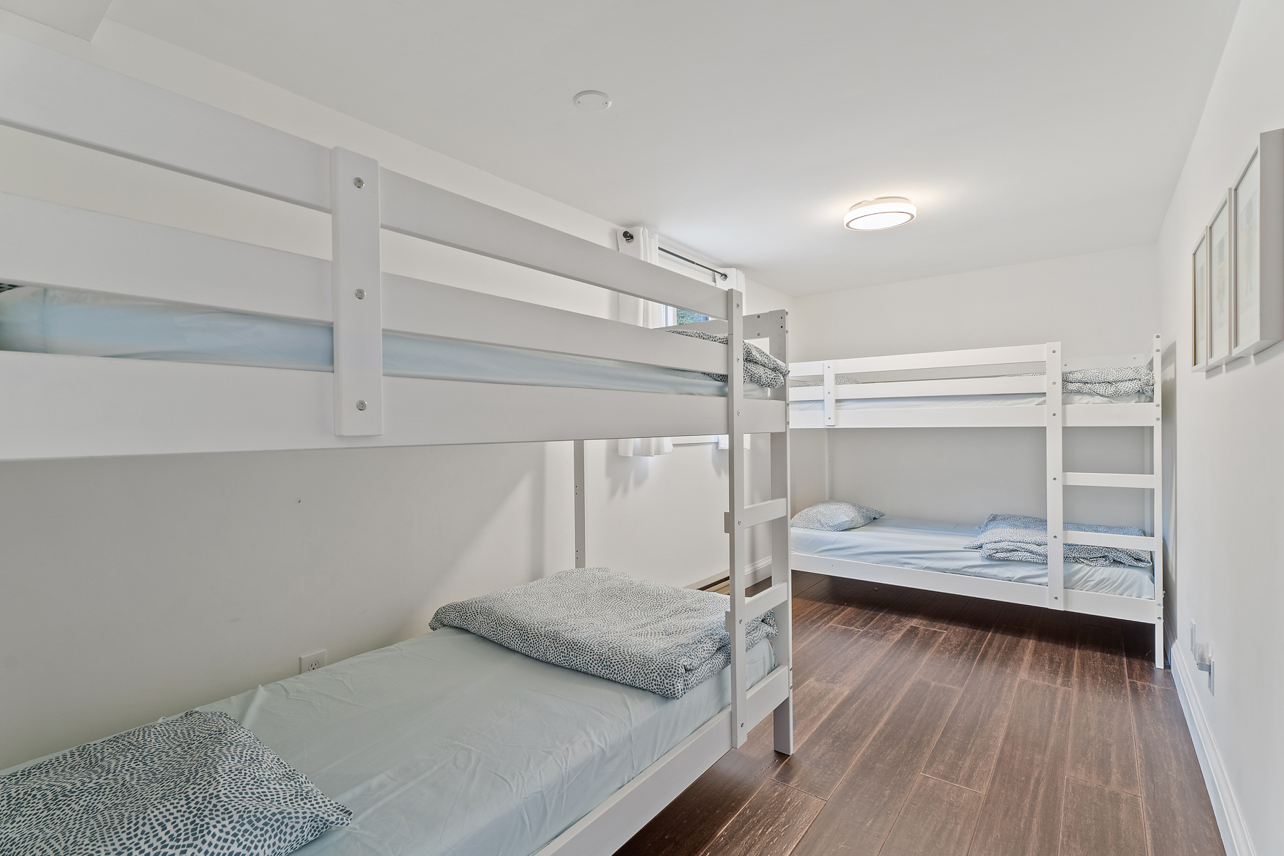 A narrow but bright bedroom with two sets of bunk beds and hardwood flooring.