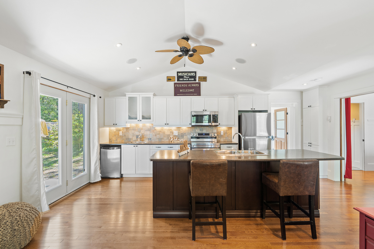 A brown kitchen island with brown bar chairs sit in front of the back of the kitchen, which features a wall of a fridge, stove, and sink