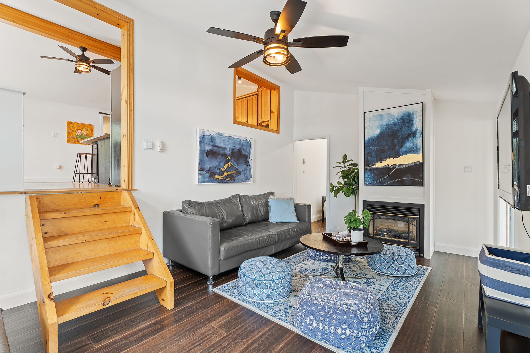 A small set of steps lead from the living area up into the dining and kitchen area. In the living room is a couch, a coffee table surrounded by beanbag seats, and a fireplace.