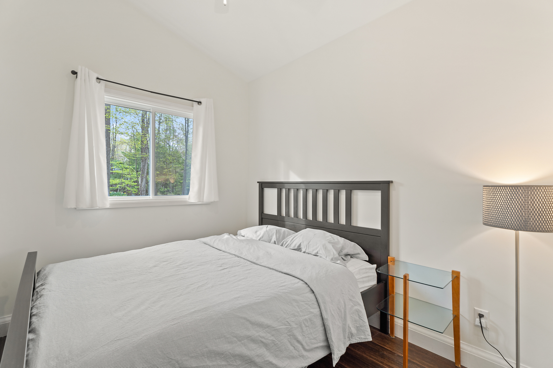 A simple bedroom with a bed, a window, and a side table.