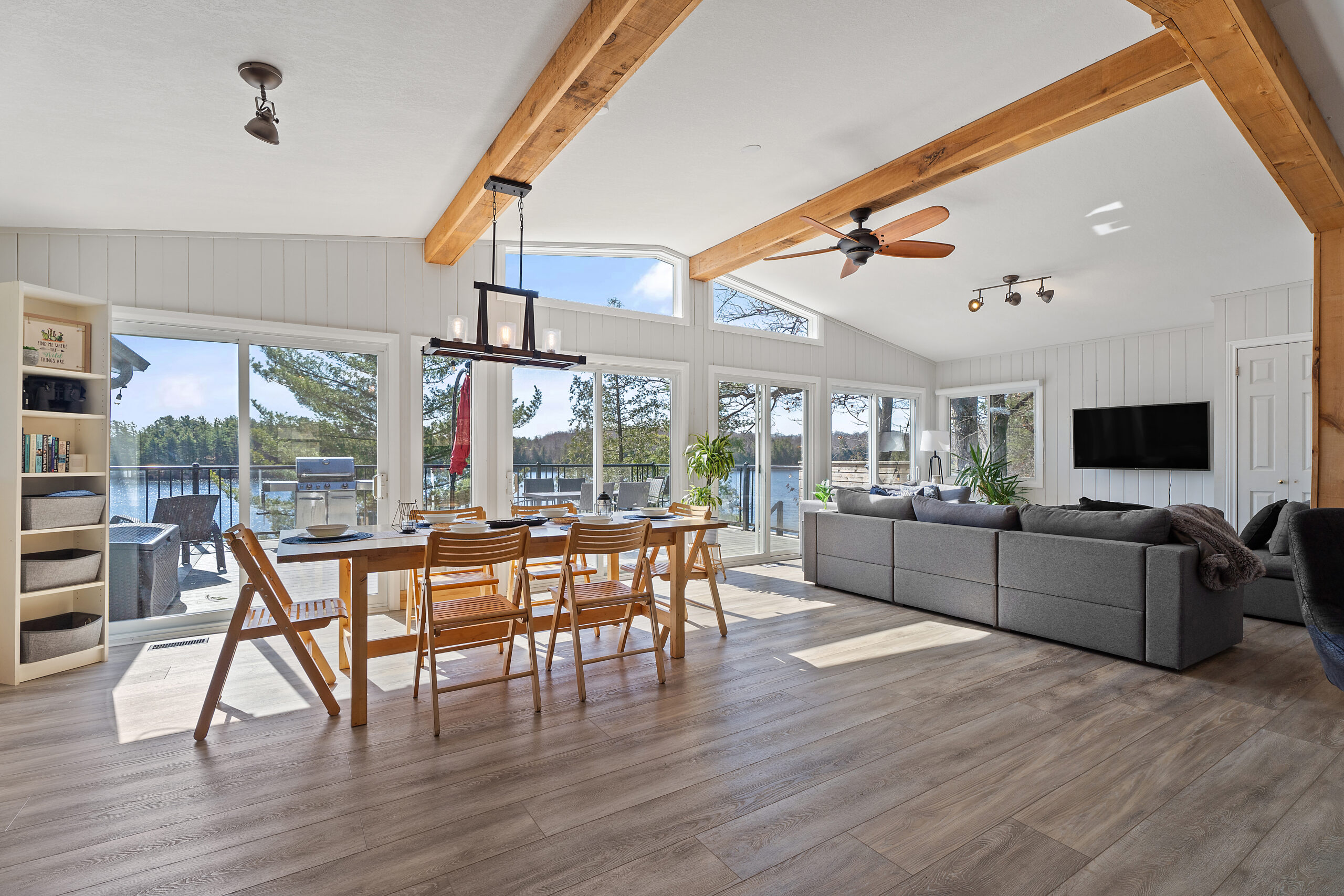 View into main living area shows brown dining table and grey couch, with large bright windows behind them
