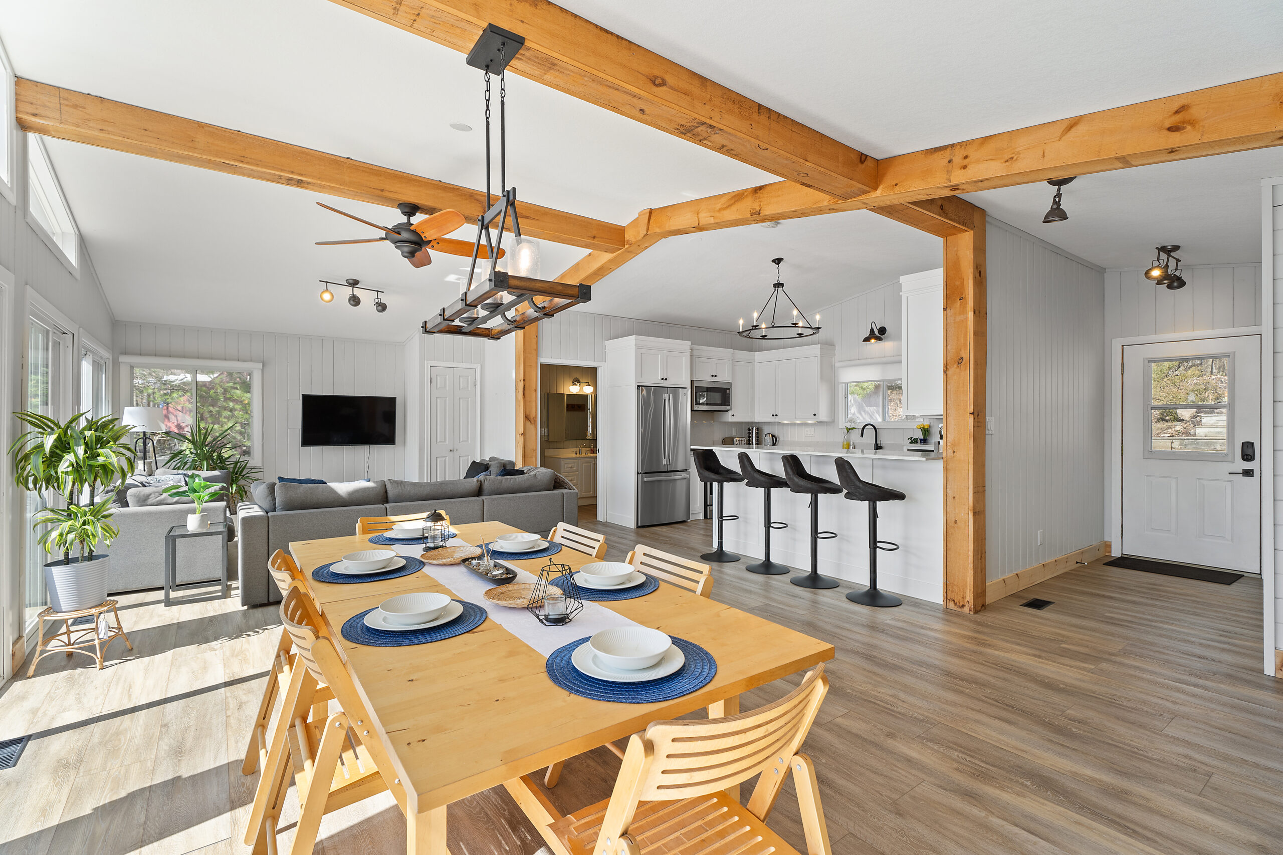 A brown dining table in front of the rest of the main living area. A grey couch and kitchen behind