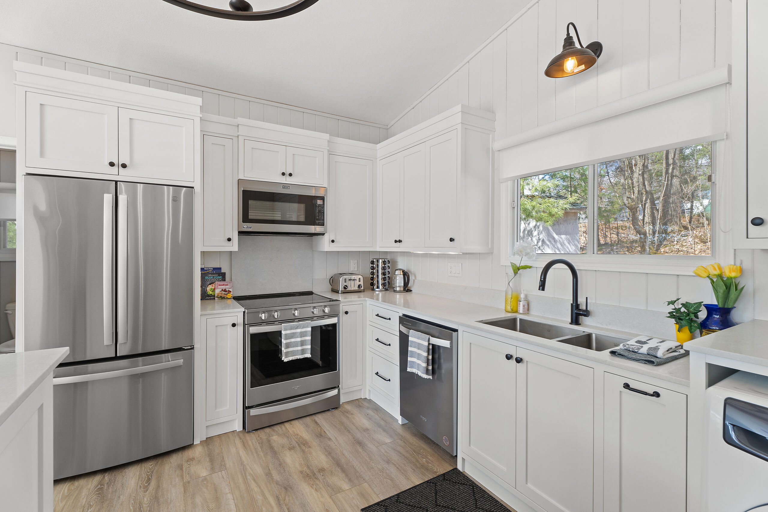 Left to right: silver fridge, silver stove with microwave above, white cabinets and sink