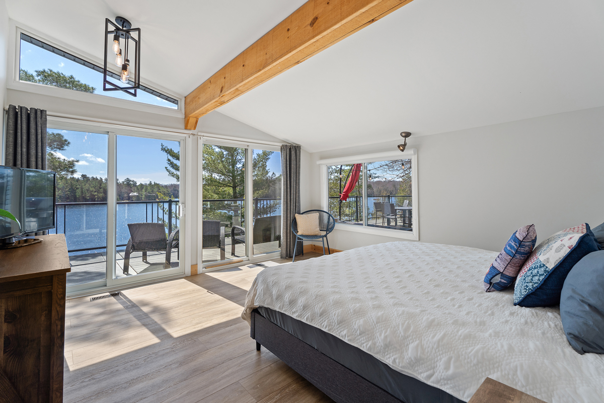 A white bed with blue pillows faces glass sliding doors onto the deck