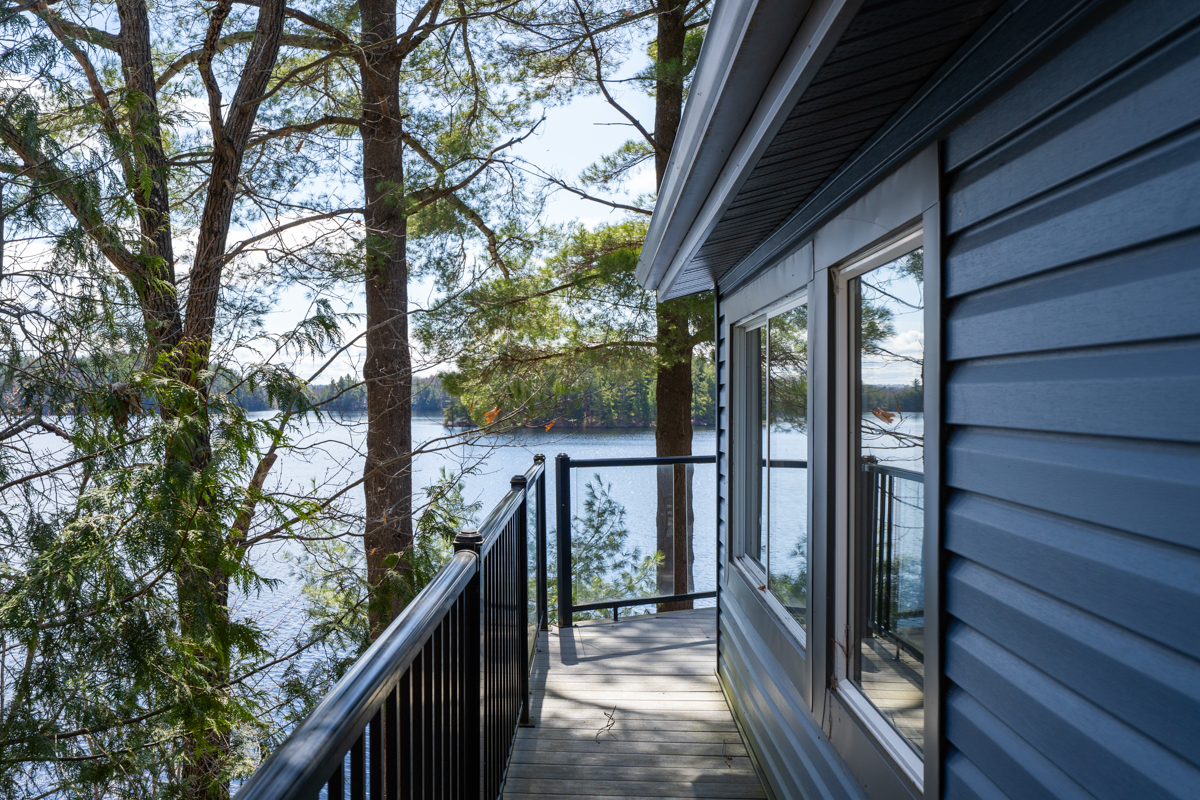 A narrow deck with glass rails along the side of the blue cottage