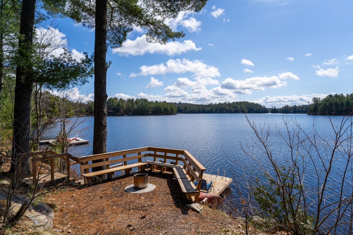 A fire pit area with wood bench seating overlooks the lake