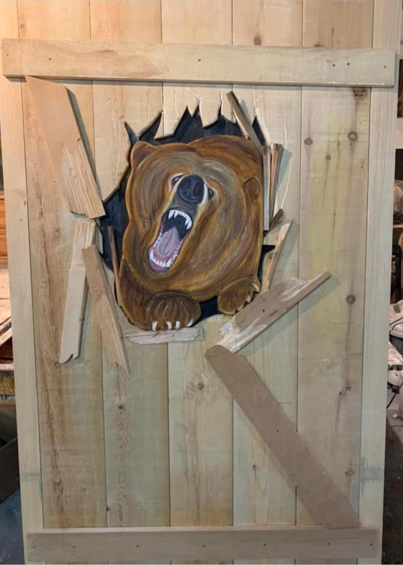 An outhouse door with a brown bear breaking out of the door