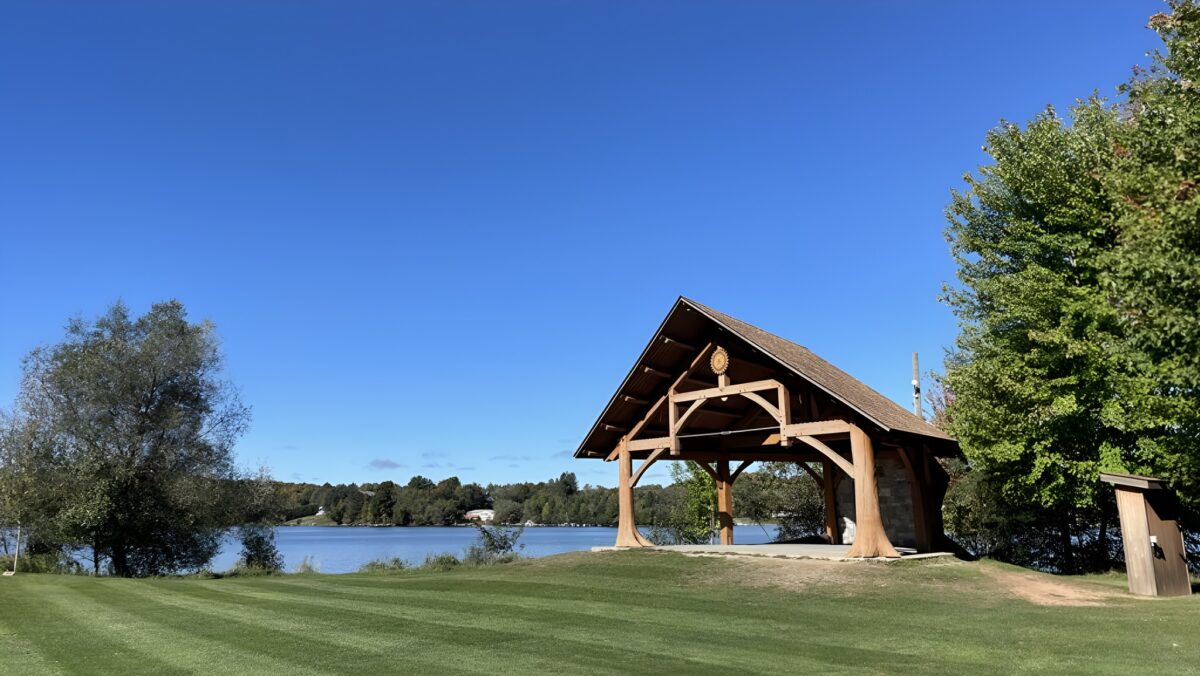 A gazebo by a wide grassy space and a lake