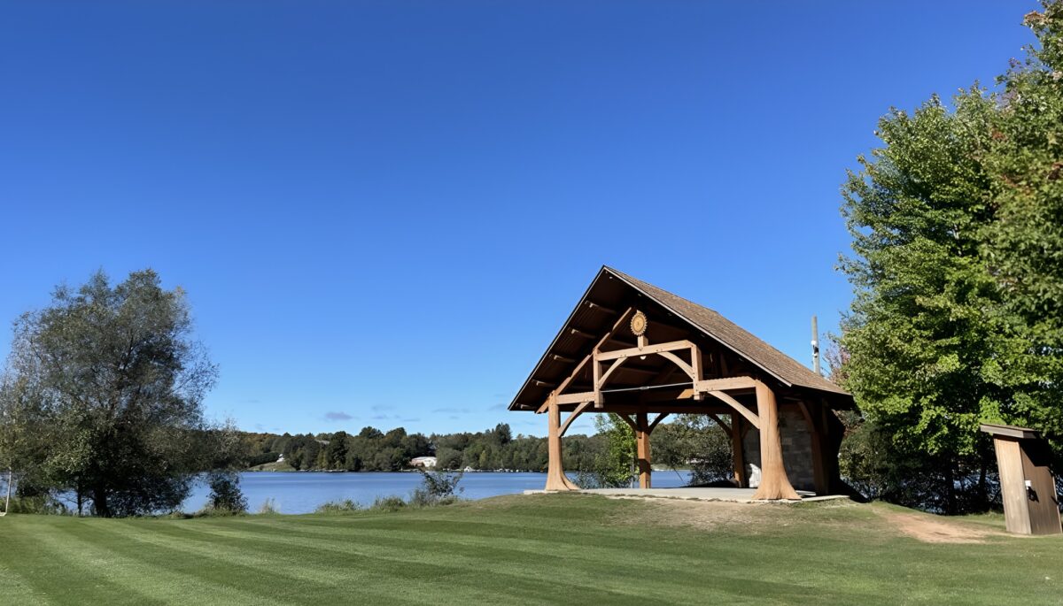 A gazebo by a wide grassy space and a lake