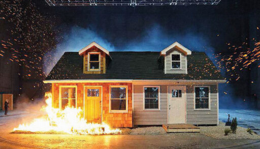 Two houses set on fire. The one with wood siding is in flames. The other house is not on fire.