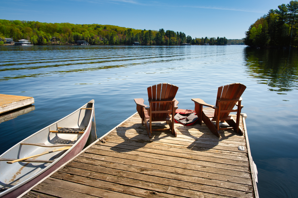 A shot of a dock with two Muskoka chairs and a canoe