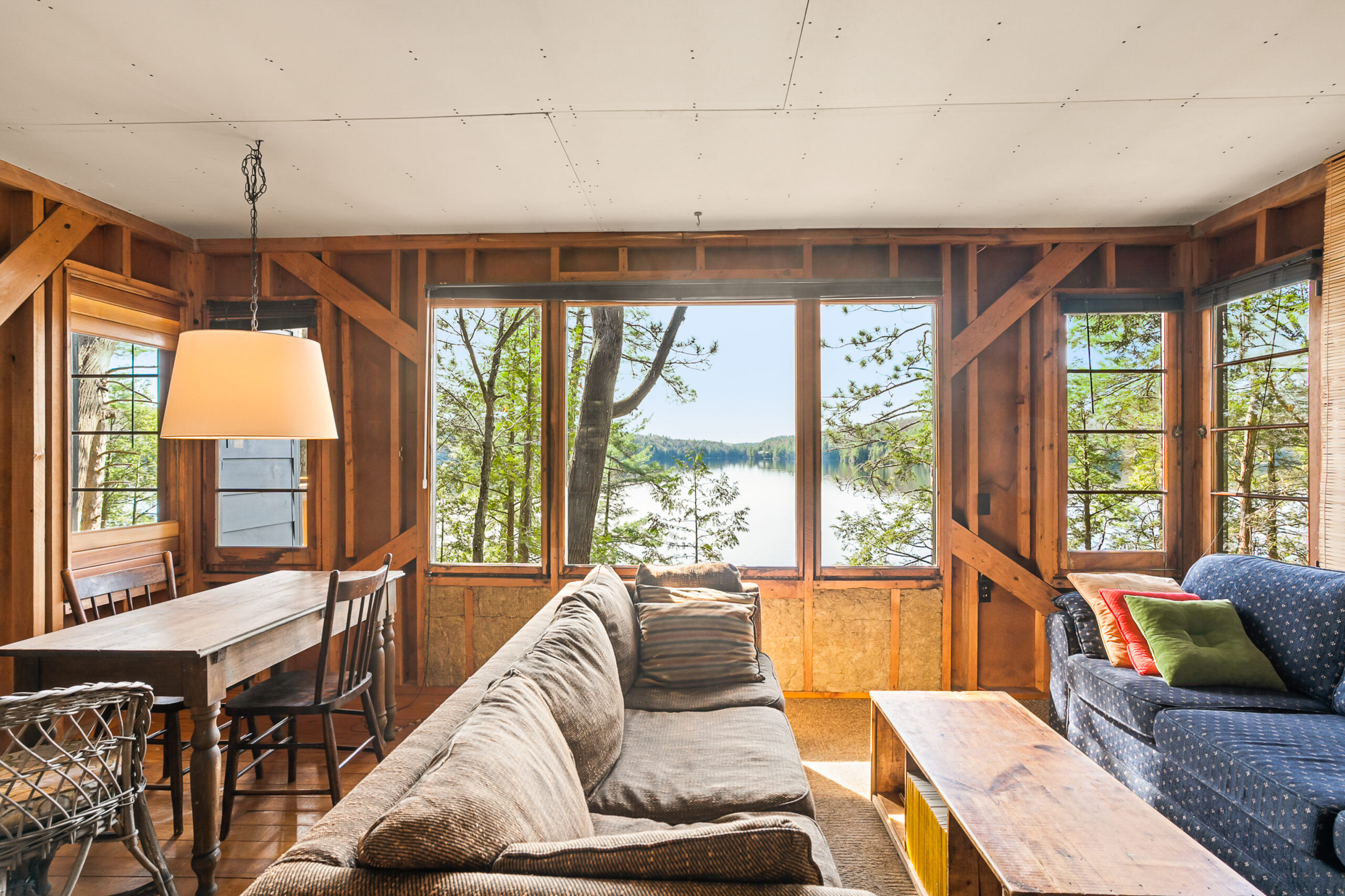A side view of a brown couch perpendicular with a wide window, with a view to the lake