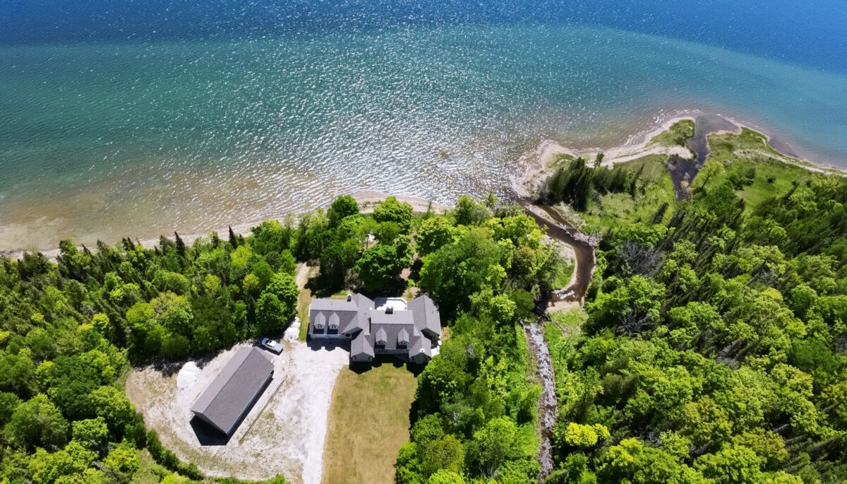A large house on a huge property surrounded by green trees. A blue lake behind