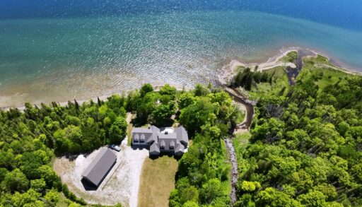 A large house on a huge property surrounded by green trees. A blue lake behind