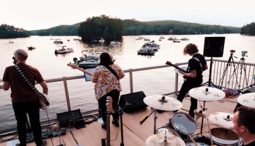 Band members preforming on a boat house with boats watching