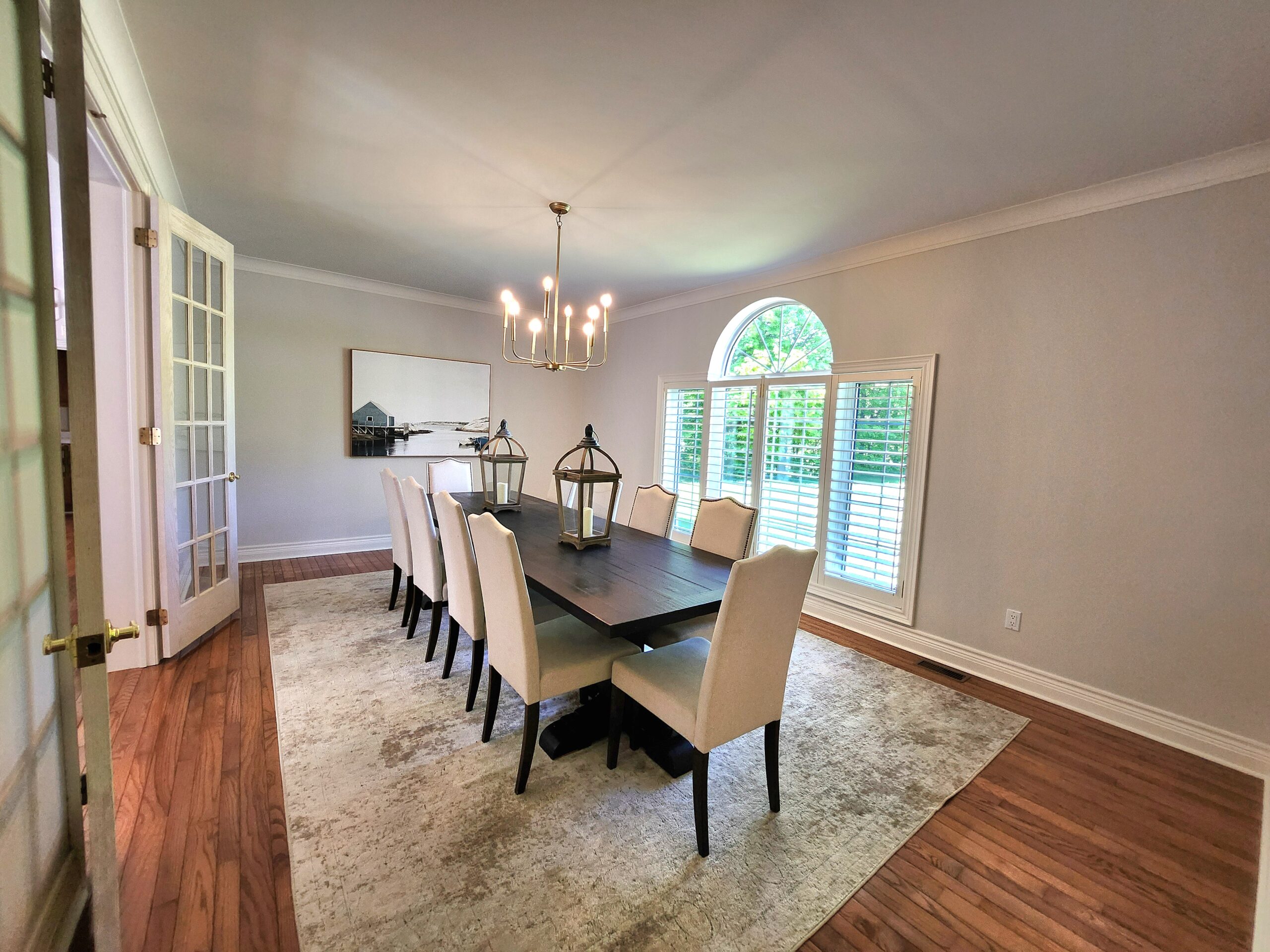 A large wood table with white dining chairs on a large white rug in a dining room