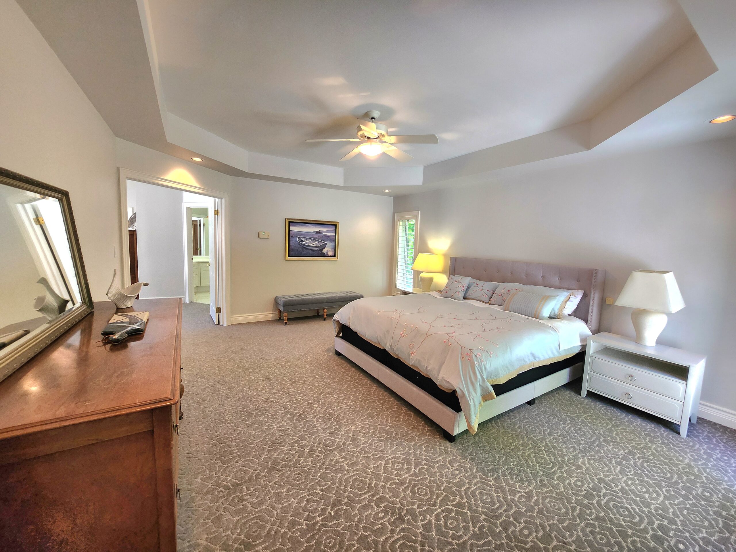 A white bed in the primary faces a brown dresser.