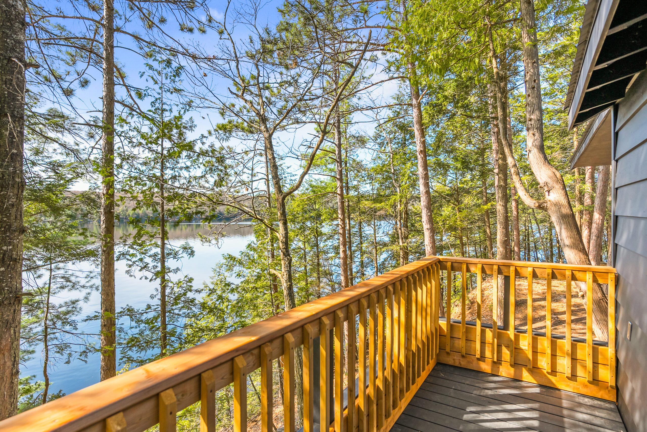 A deck with wood rails looks out to the tree covered lake