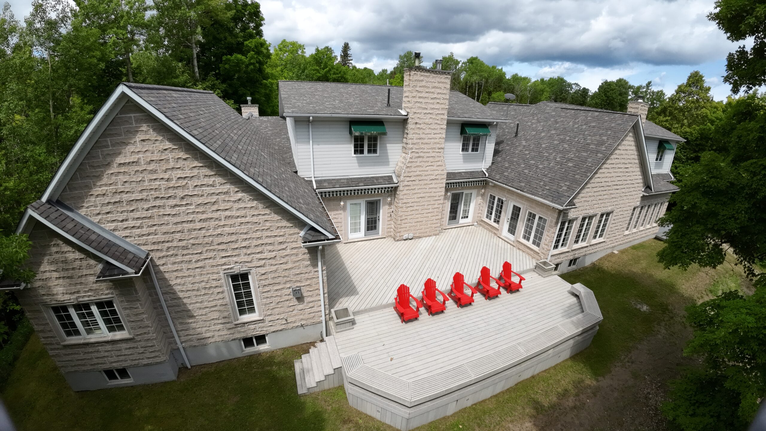 The back deck sits between the house's L-shaped structure. Five red Muskoka chairs are on the edge of the deck and face away from the house
