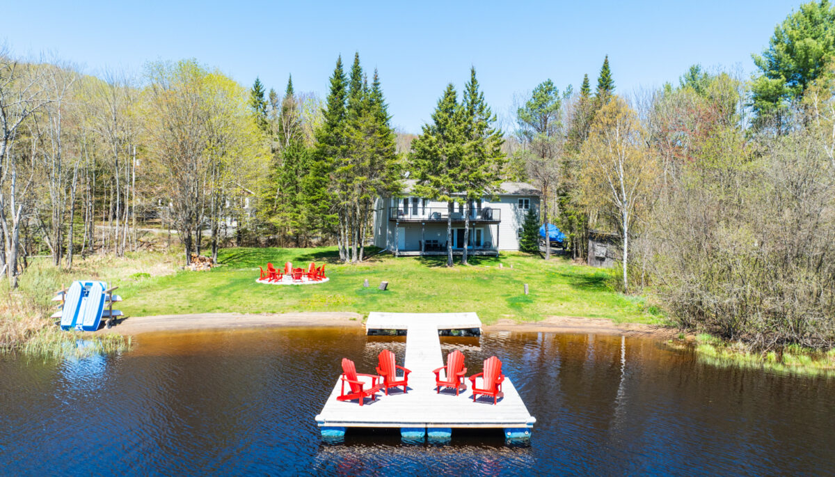 View from the front of the dock. The dock backs up onto wide greenspace and the brown cottage is nestled in the trees behind
