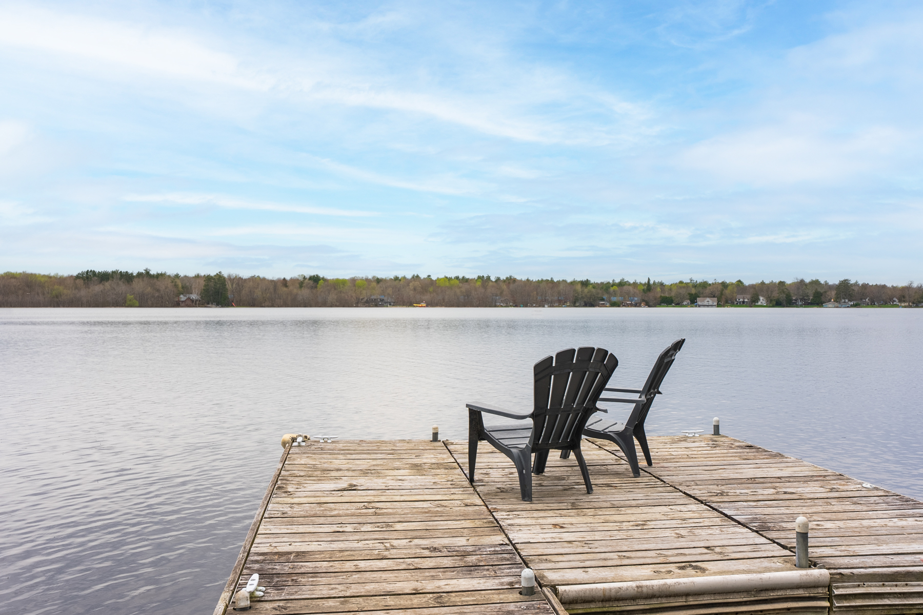 Two Muskoka chairs sit on the end of a wooden dock, looking out across a still lake.