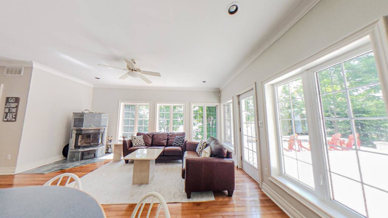 White walls and large windows surround the family room. Two brown leather loveseats on a white rug face a coffee table
