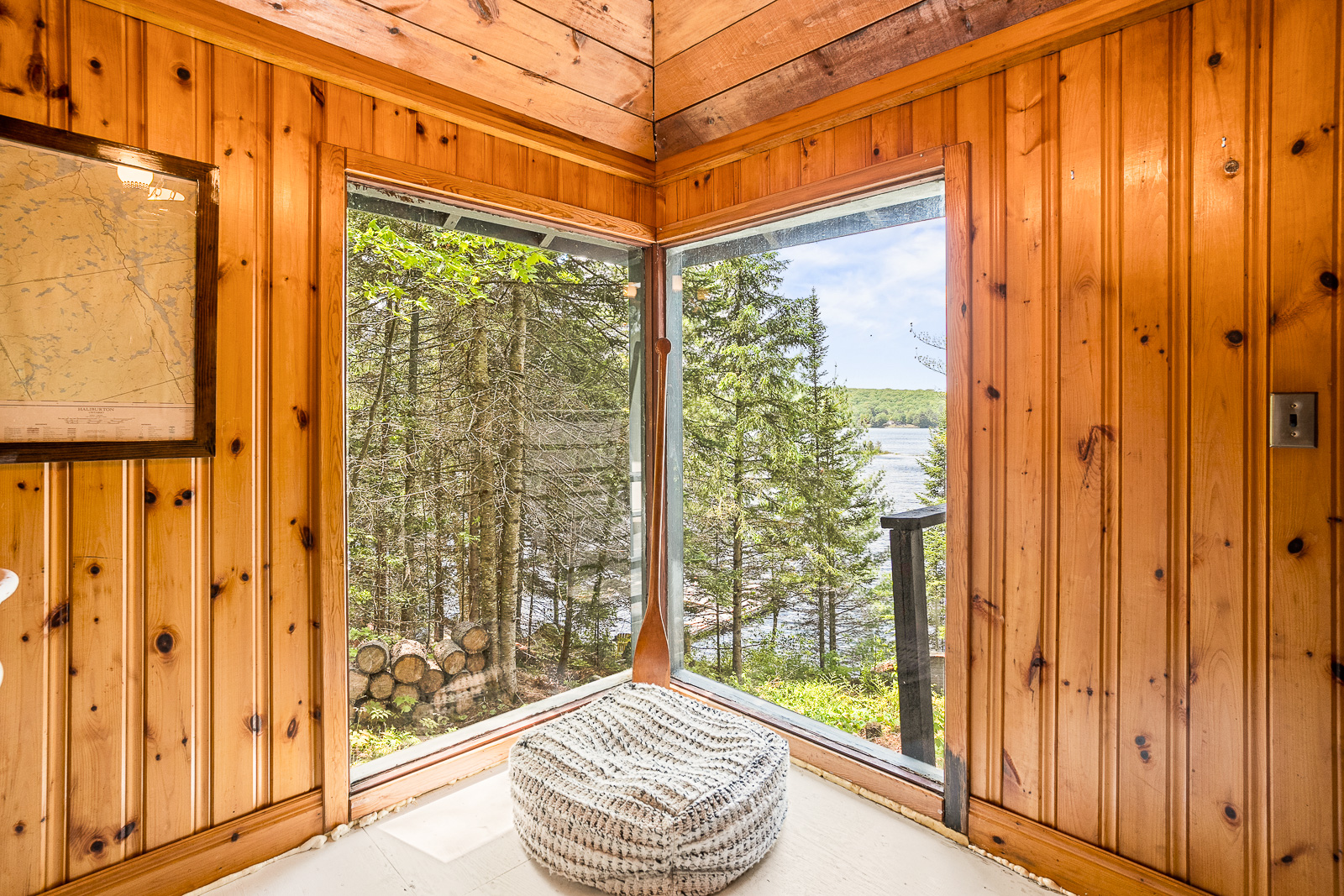 a corner of the cottage with large windows that meet at the corner. A small cushion sits on the floor