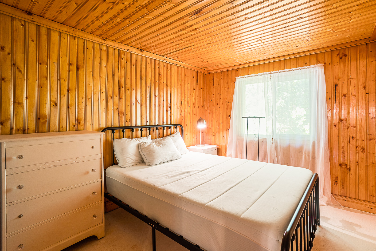 A wood-paneled bedroom with a simple white bed