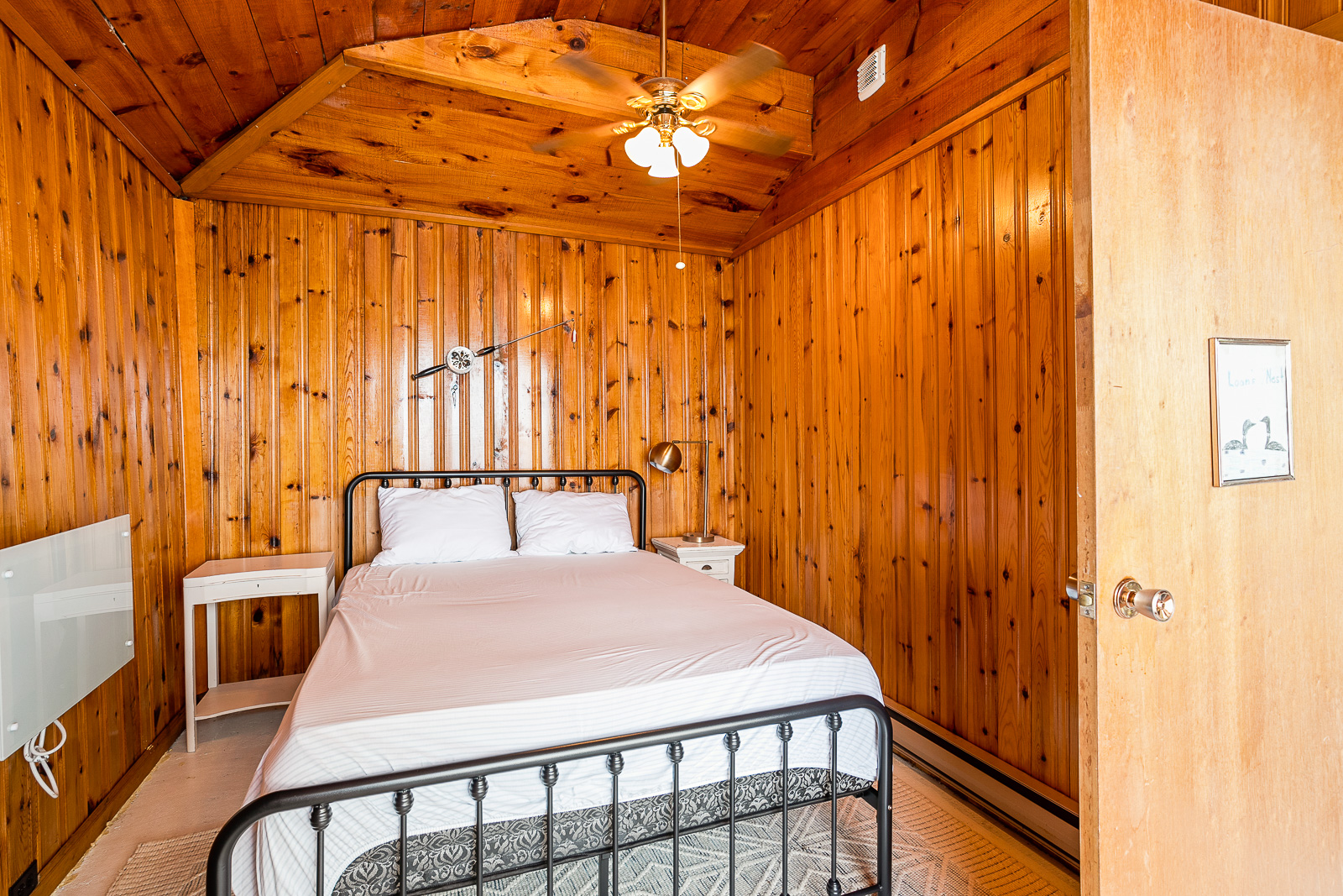A brown paneled bedroom with a simple white bed and iron-bedframe