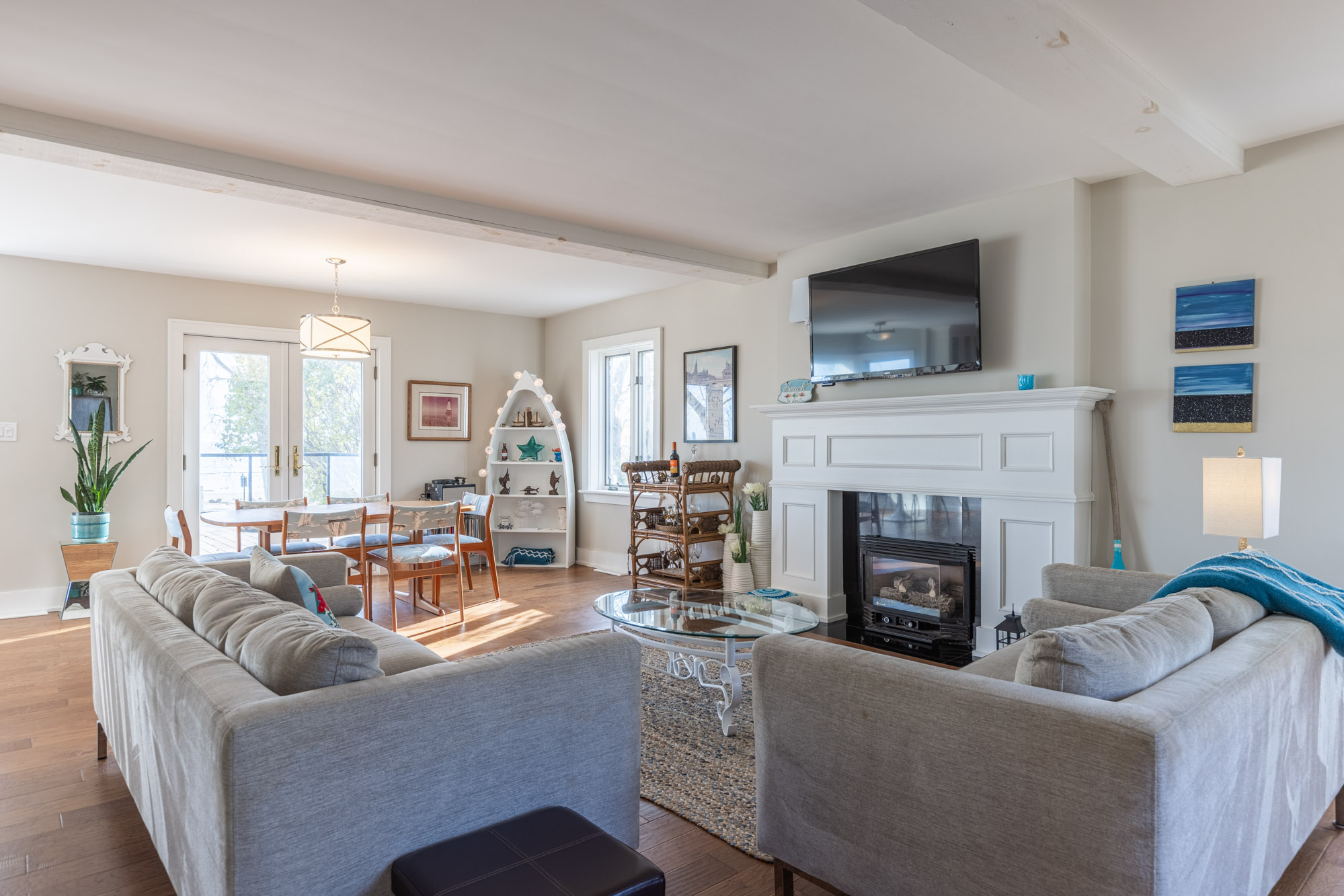 The living area features perpendicular beige couches. One couch faces a small table, fireplace and a TV hanging ont he wall