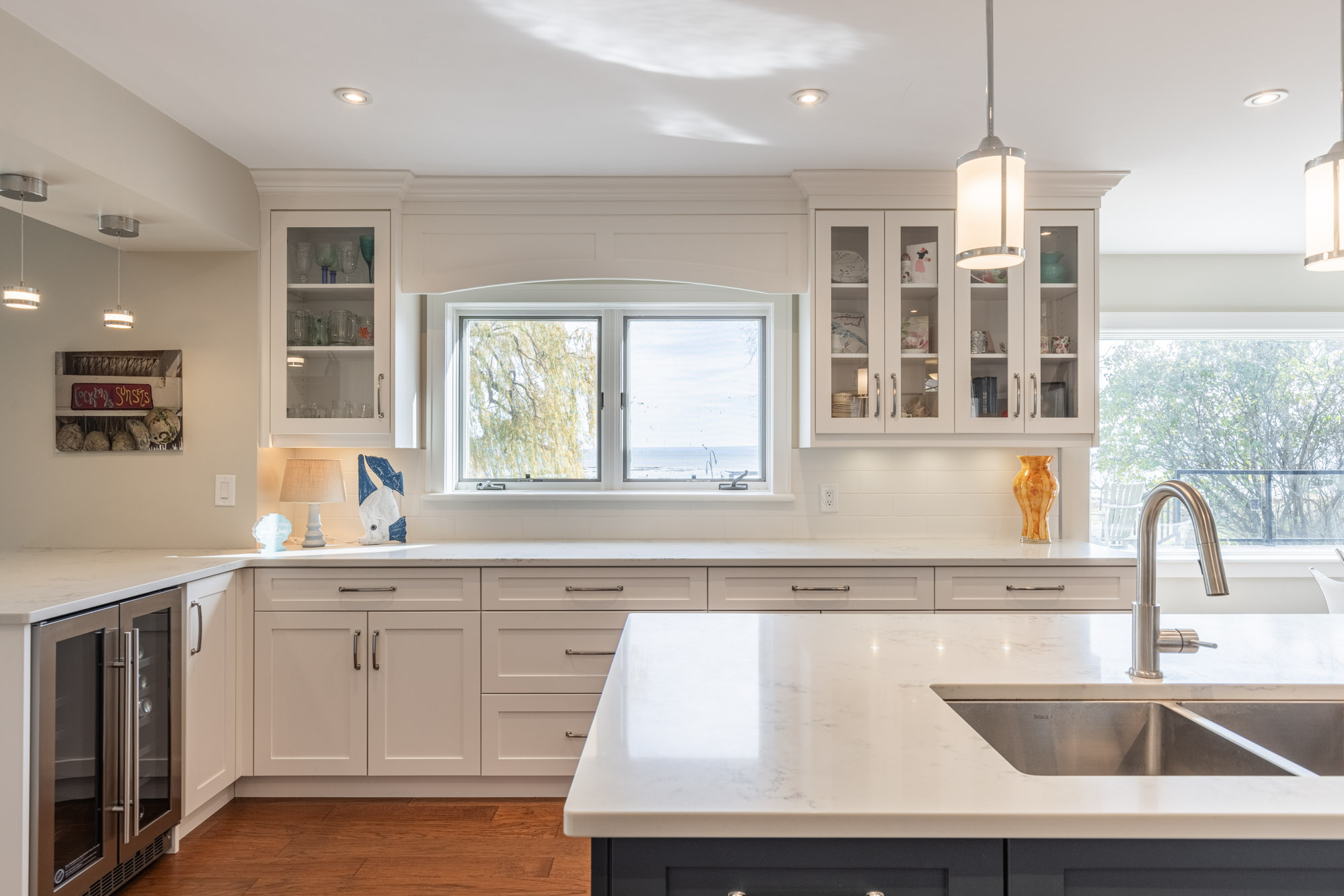 Another side of the kitchen is lined with white cabinet with a large windows. The kitchen island has a large sink
