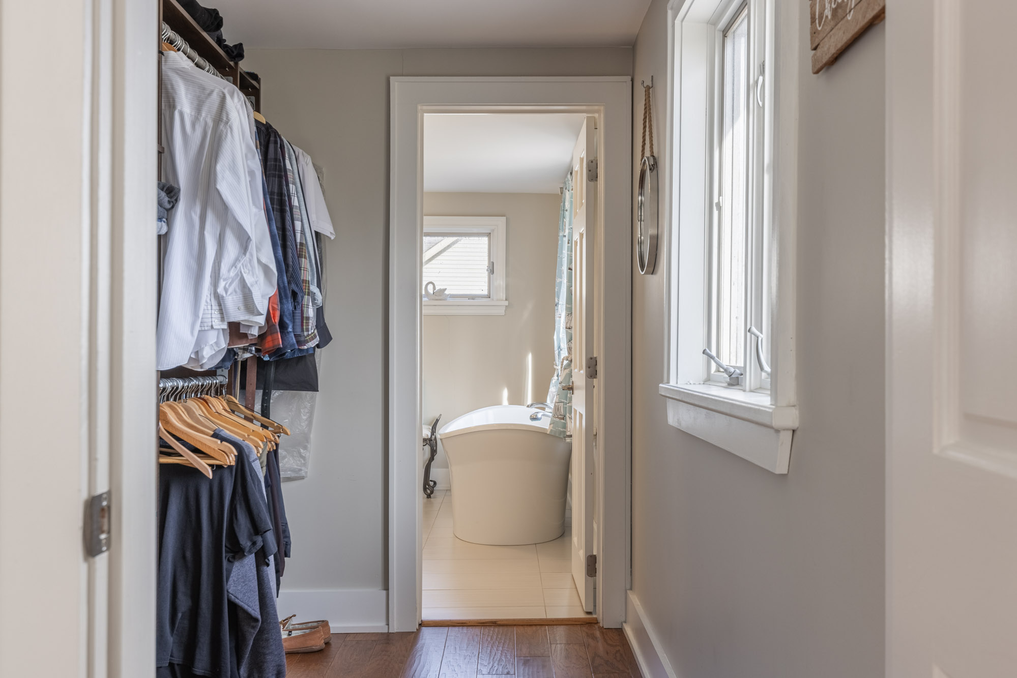 Clothes hang in a closet to the left and faces a window. In the middle is a doorway to the bathroom