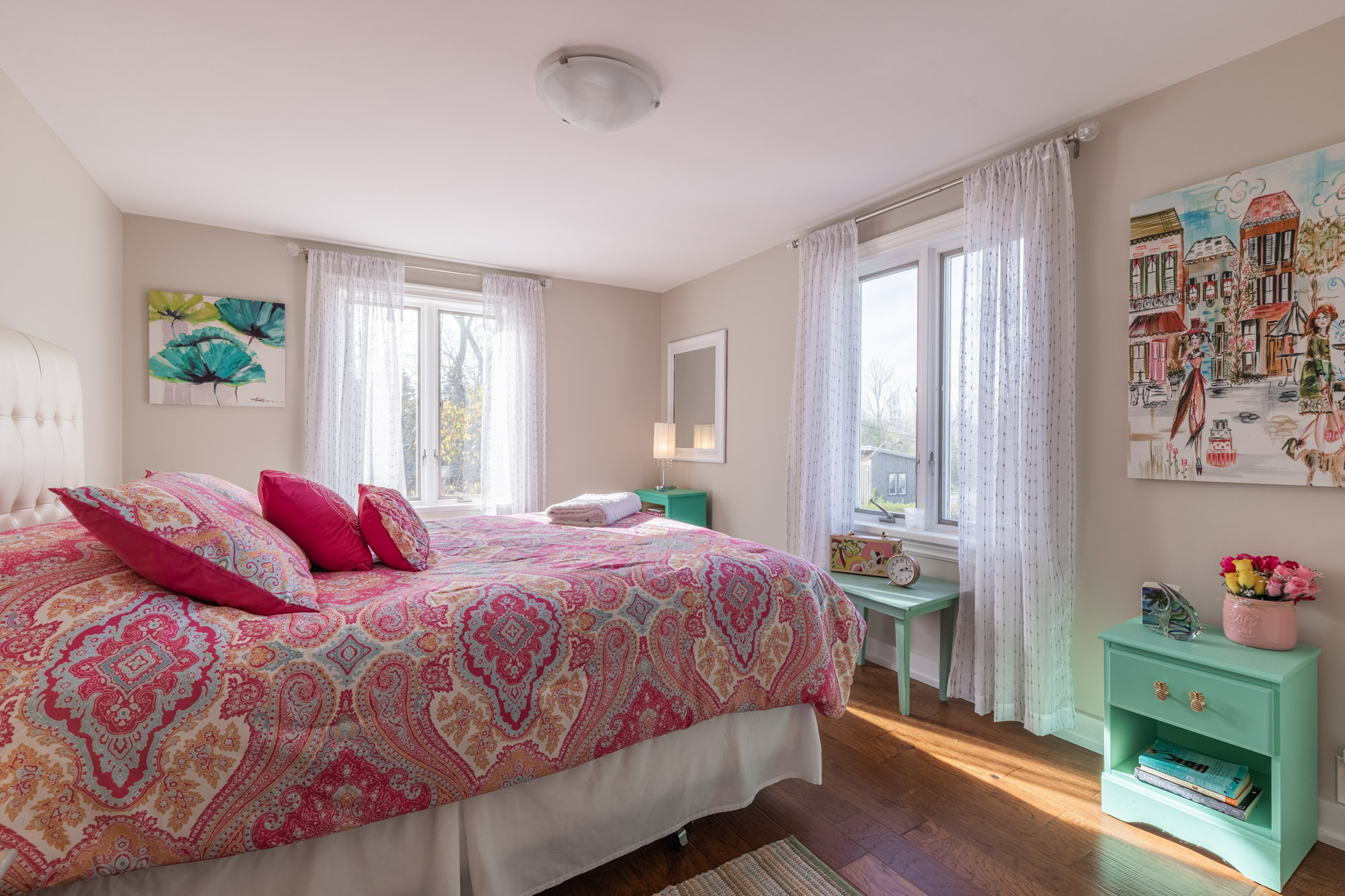 A pink bed faces windows with white curtains