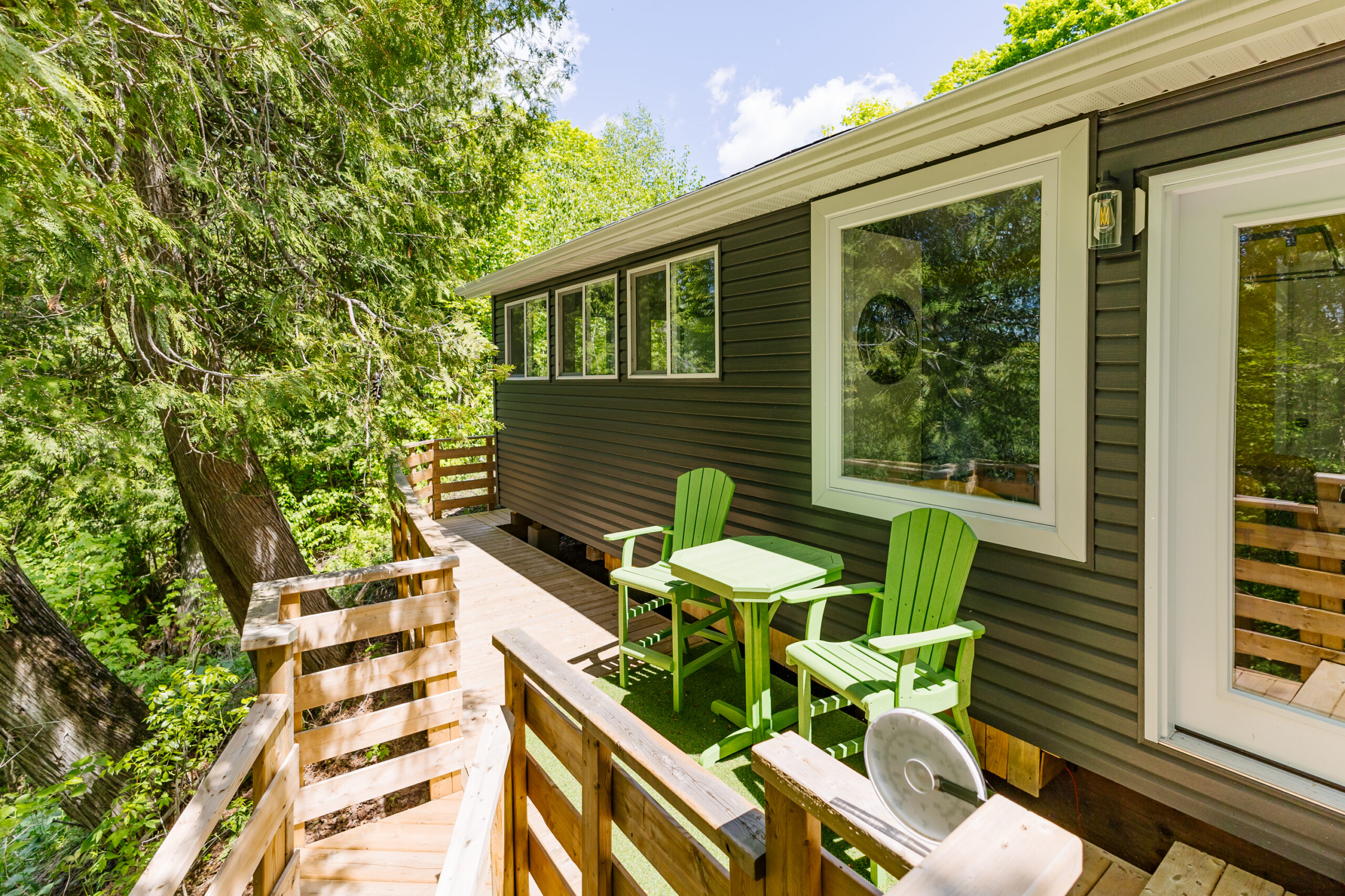 Green chairs and a small green table next to the main cottage on the back deck