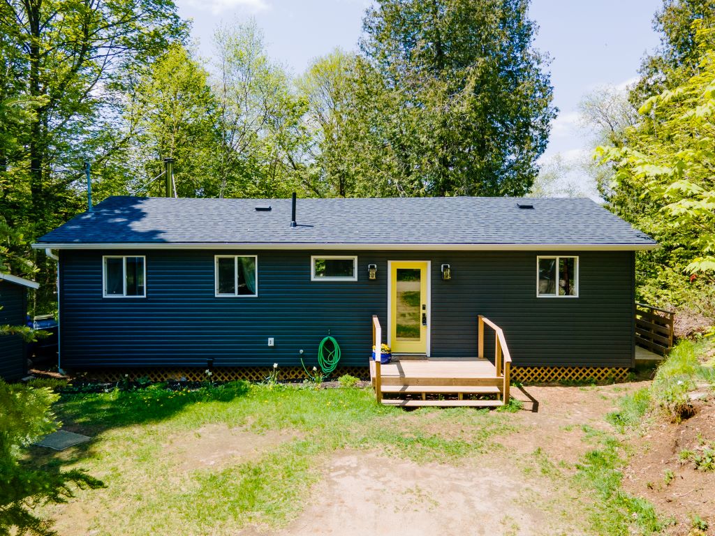 A blue-grey panelled bungalow with wood streps that lead to a bright yellow door
