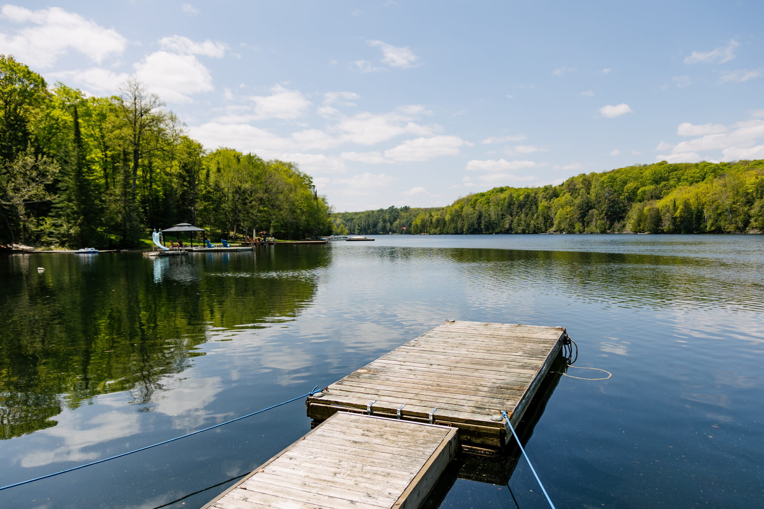 A dock floats in the blue water. Tree lined islands in the distance
