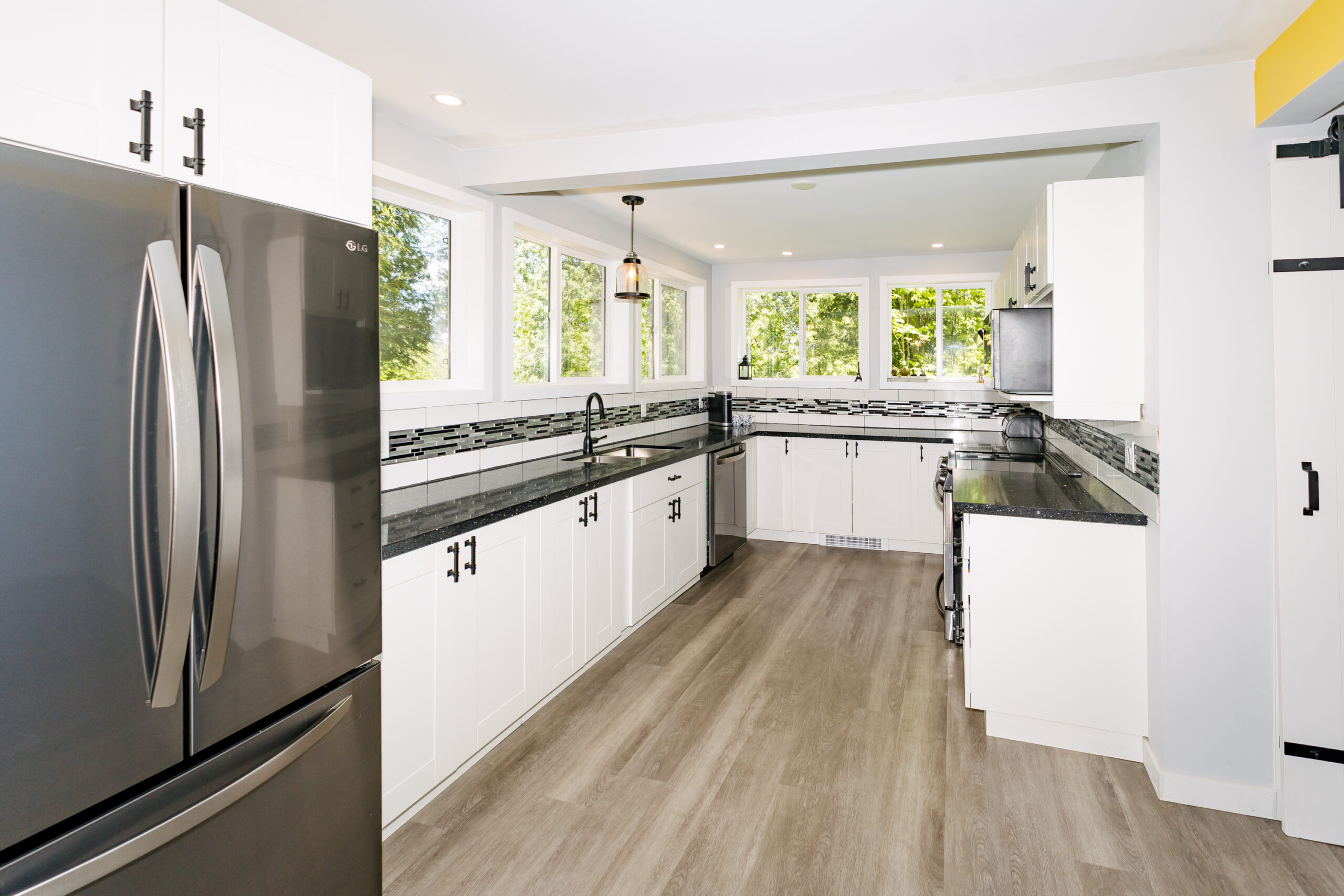 Facing the kitchen, a stainless steel fridge on the left. Wraparound kitchen cabinets with black countertops. Windows above the counters