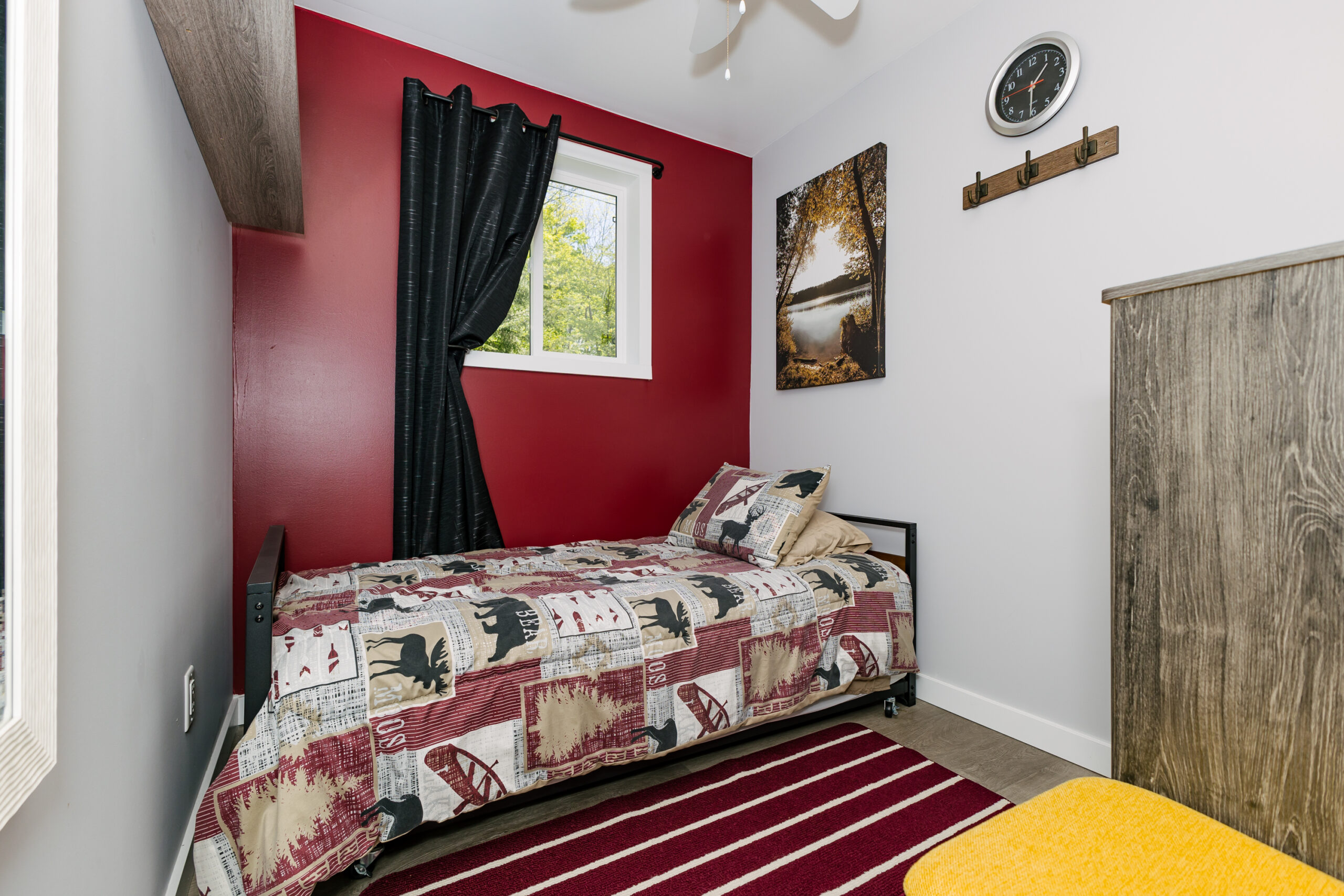 A red and brown bed pressed against a red wall with a black curtain. On the ground, a red and white striped carpet.