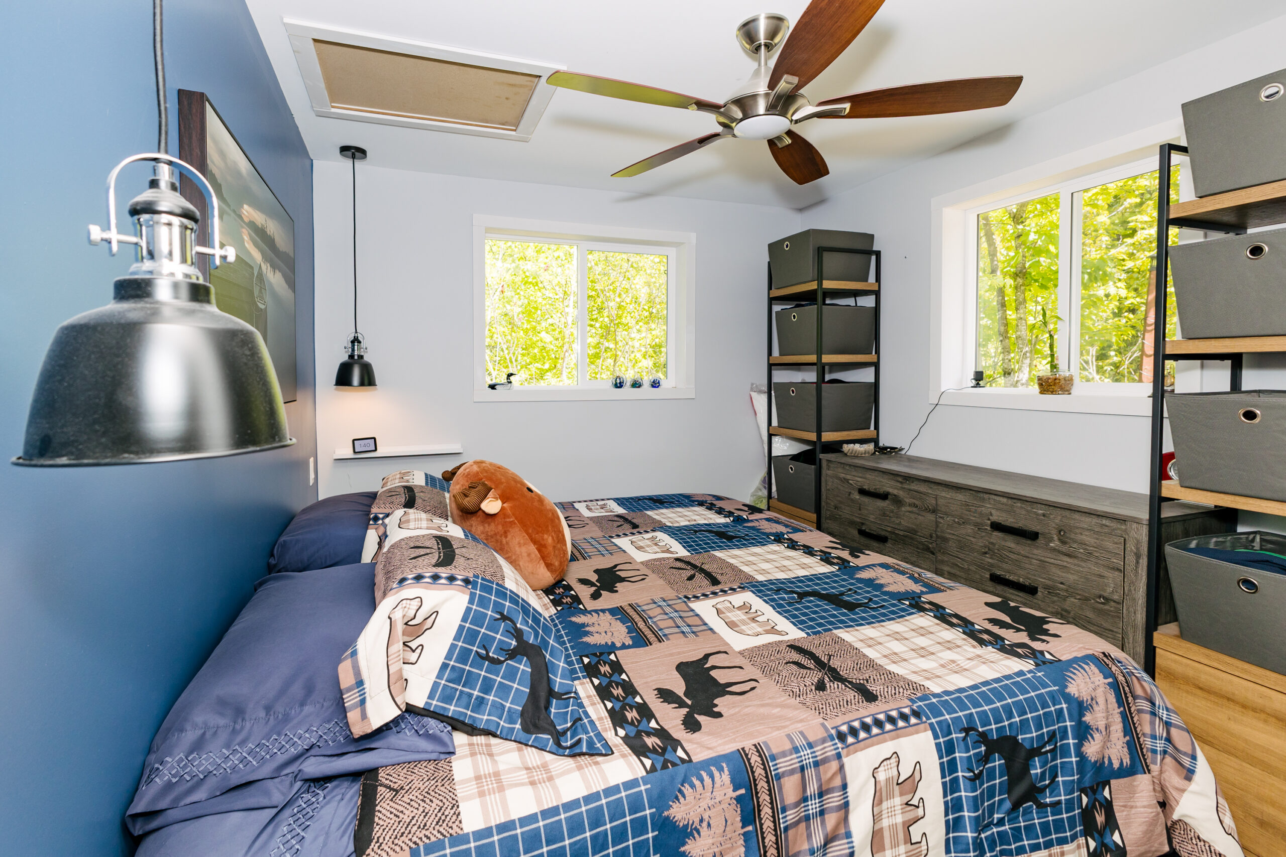 Side view of a bed with a blue and brown bedspread. The bed faces a window