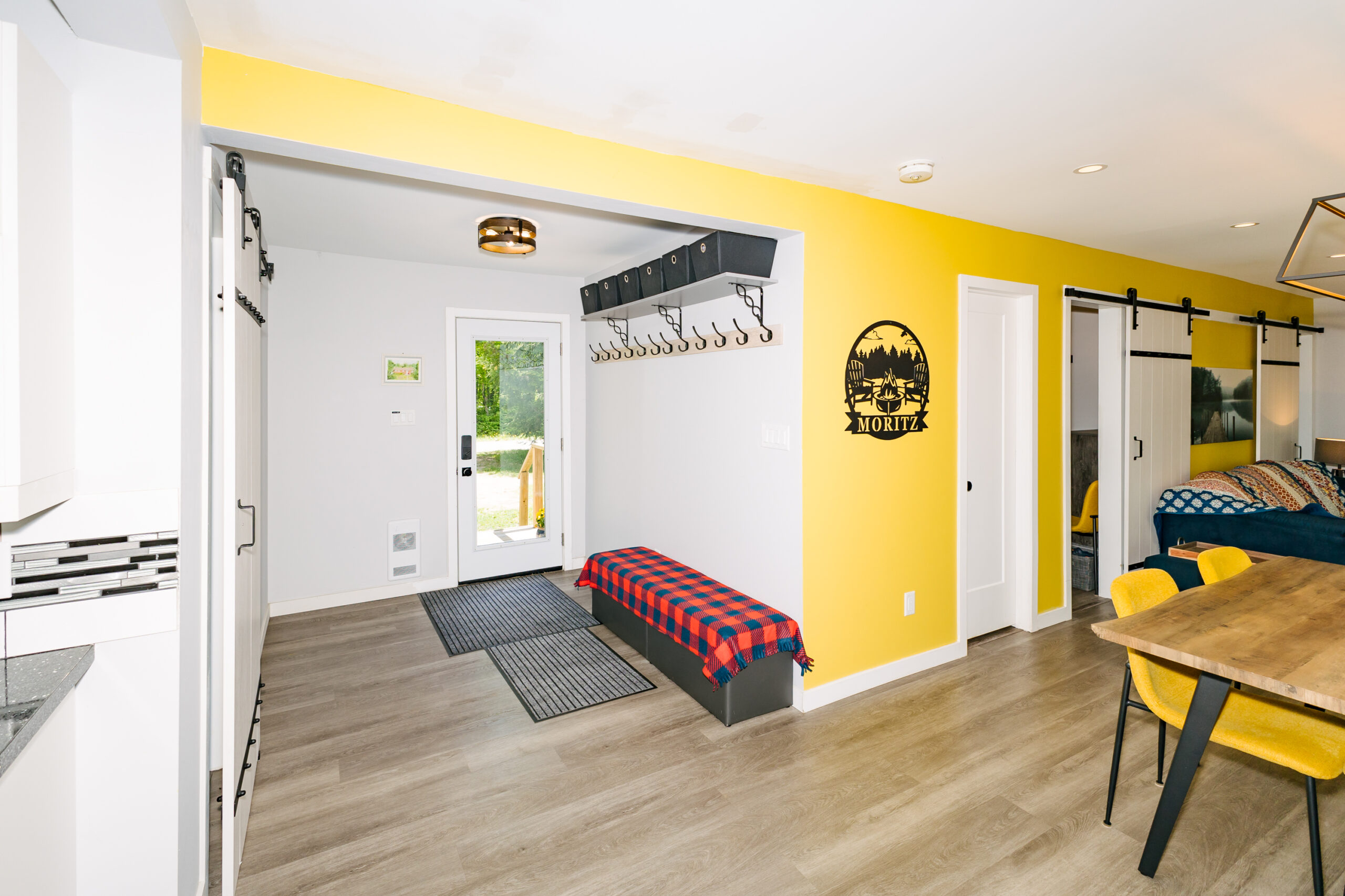 A white entryway with a long black bench covered in a black-and-red checked blanket. An adjoining wall is painted yellow